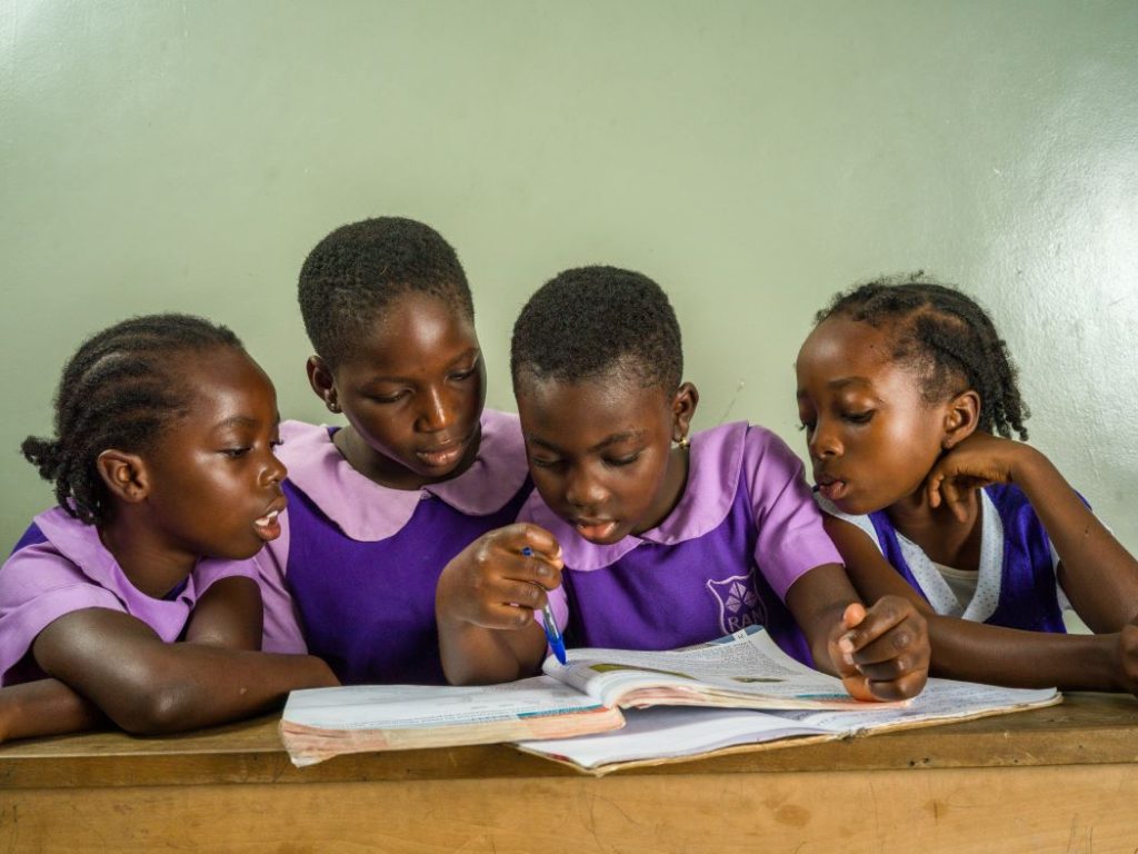 Girls wearing Rising Academies uniforms looking at a book and demonstrating the value of education in Ghana.