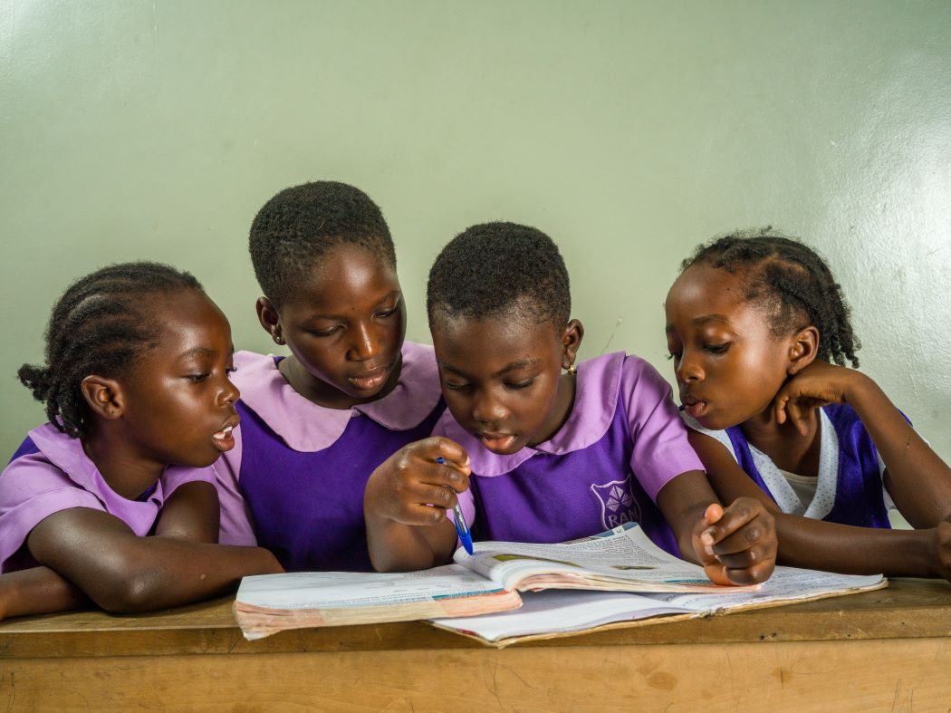 Girls wearing Rising Academies uniforms looking at a book and demonstrating the value of education in Ghana.