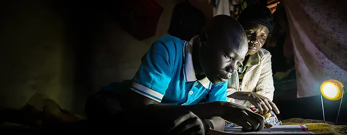 Boy studying with woman under a small lamp light.