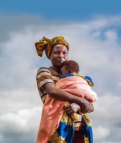 Woman holding child wrapped in colorful blanket against cloudy sky.