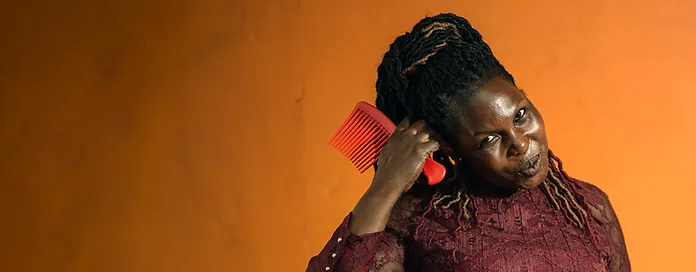 Woman combing her hair with a red comb against an orange background.