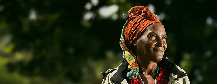 Elderly woman in headscarf smiling against a green, blurred background.