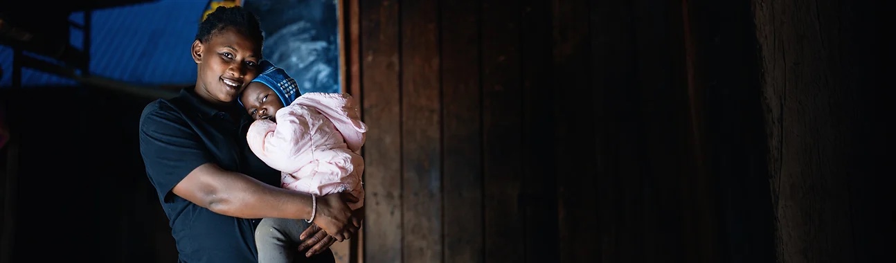 Smiling woman holding a baby indoors.